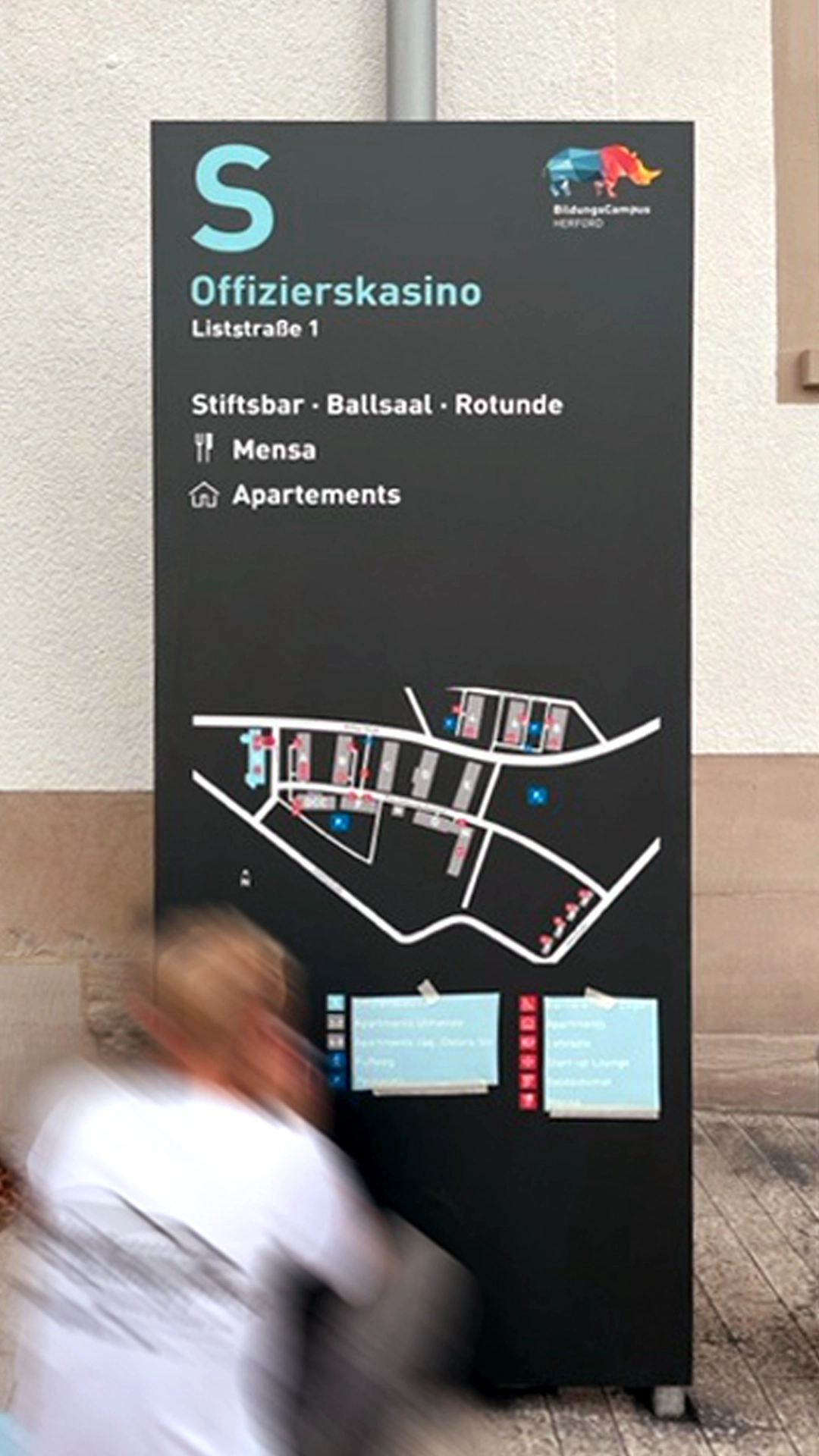 Leitsystem-Stele auf dem SEH-BildungsCampus Herford mit Standortangabe „Offizierskasino“ und Übersichtskarte des Campus, gestaltet im Rahmen eines Wegeleitsystems, das die militärische Vergangenheit des Geländes mit seiner neuen Nutzung verbindet