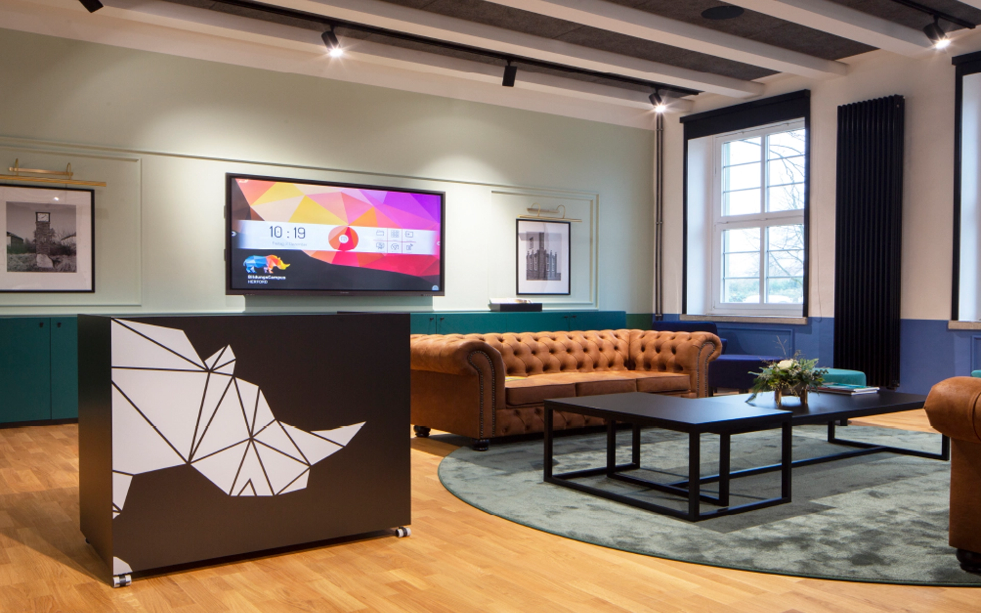 Aufnahme der räumlichen Markenanwendung für den SEH BildungsCampus Herford: Logo im Anschnitt auf Glastüren, im Hintergrund Blick in die Lounge.