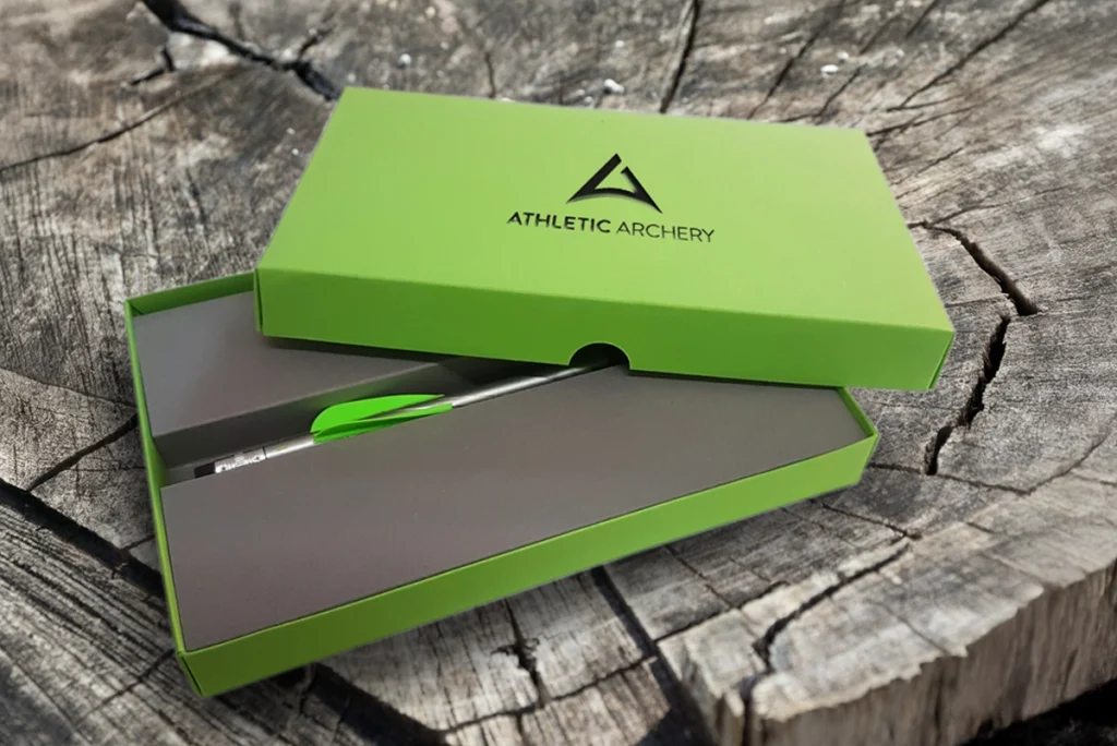 Produktaufnahme des Mailings für athletic archery mit gestalteter Verpackung und einem individuell gefertigten Stift, veredelt mit einer für den Bogensport typischen Befiederung. Gestaltung durch R211-Agentur.