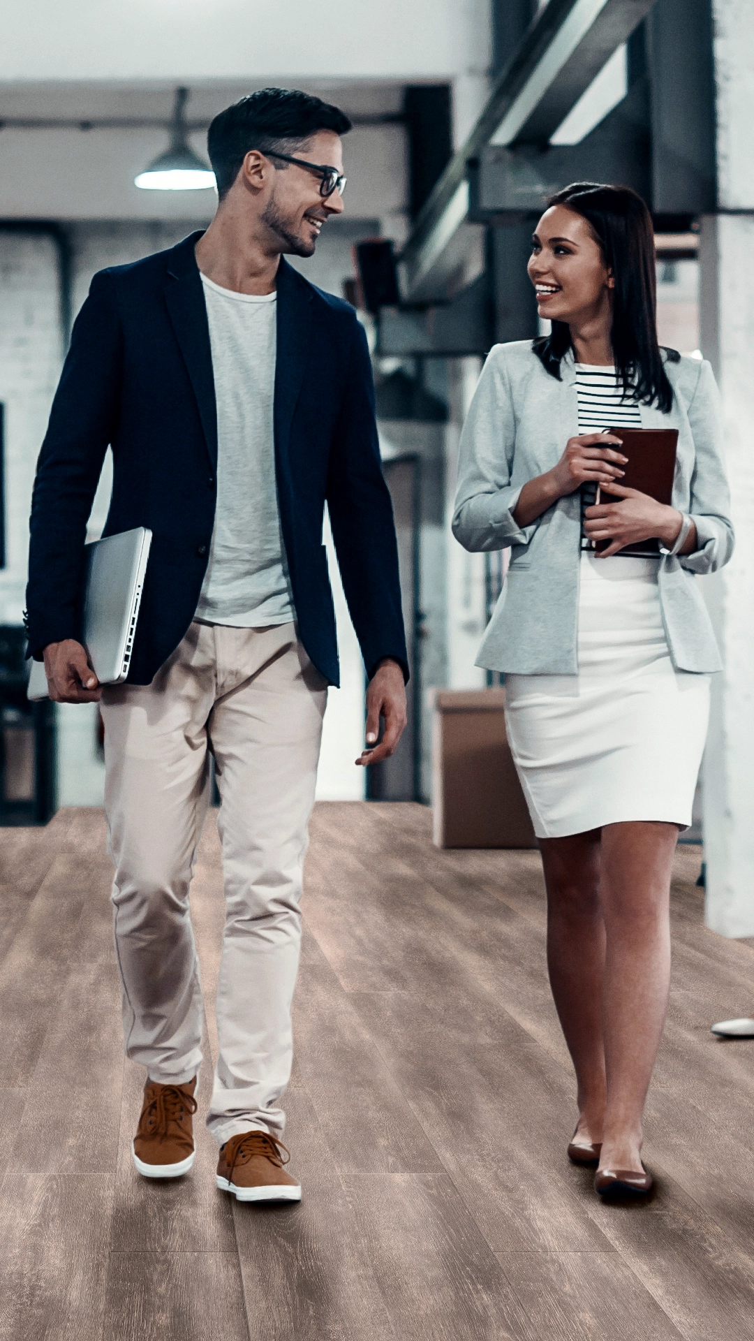 B2B-Mailing für amtico Bodenbeläge, Motiv mit zwei Businesspersonen gehen lächelnd durch ein modernes Büro mit braunem Vinylboden