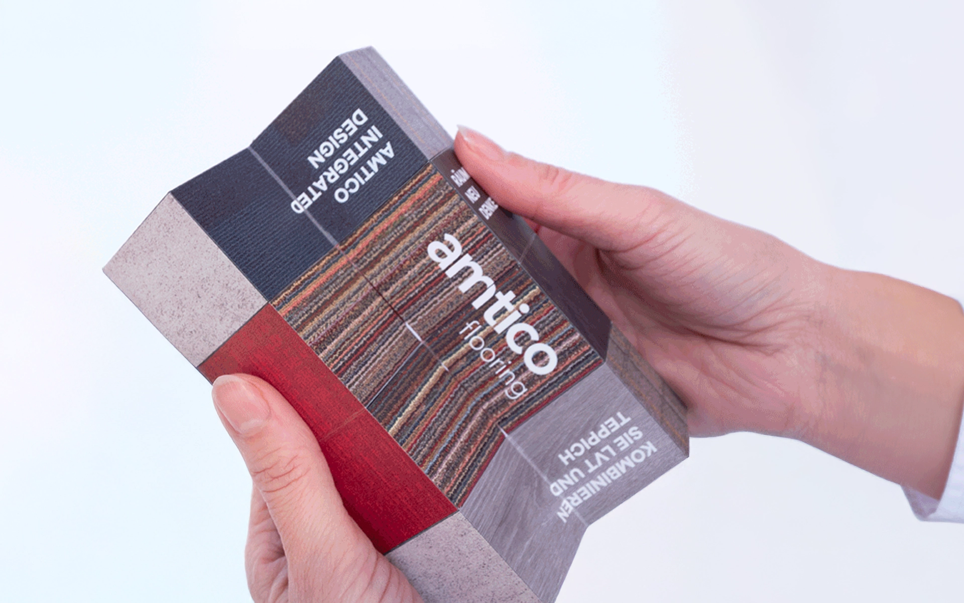 B2B-Mailing für amtico Bodenbeläge mit aufgefaltetem Würfel, gehalten von zwei Händen, mit Materialmustern aus Teppich und Vinyl