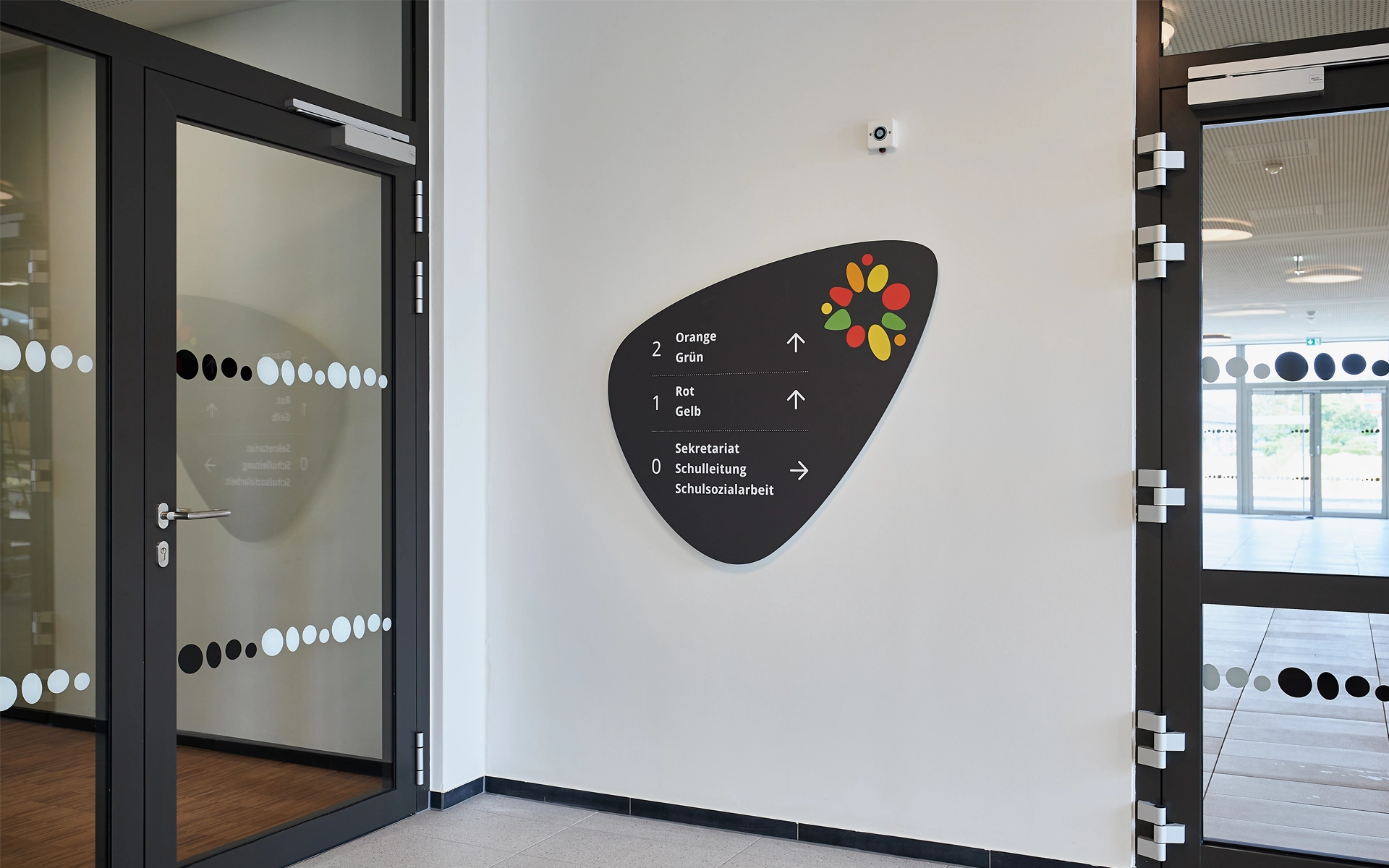 Wandbeschilderung im Eingangsbereich der Grundschule „Im Pfingsterfeld“ mit farbcodiertem Wegeleitsystem und organischer Form, gestaltet von R211 zur Orientierung auf drei Etagen
