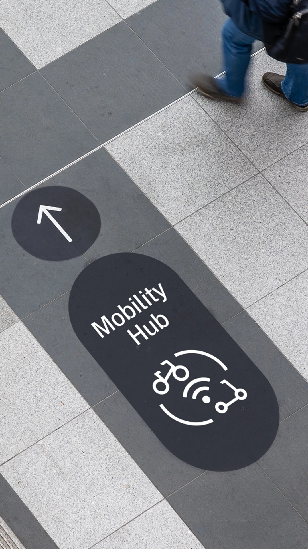 Nahaufnahme eines Piktogramms für den Mobility Hub der Deutsche Bahn, das den Übergang von Bahnreisen zu Mikromobilität wie E-Roller oder Fahrrad symbolisiert – auf dem Boden. Gestaltung durch die R211-Agentur.