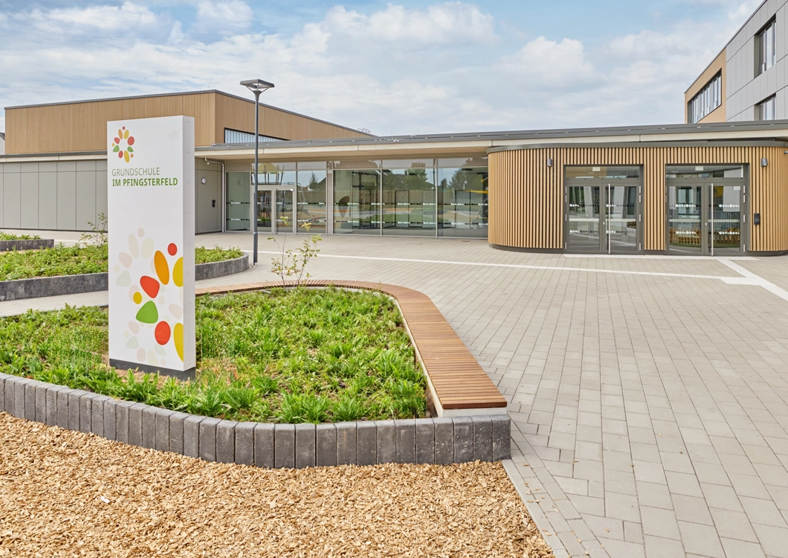 Außenaufnahme des Eingangsbereichs der Gesamtschule Waldschlösschen in Velbert mit Leitsystem-Stele im Vordergrund und Schulgebäude im Hintergrund. Umsetzung in Zusammenarbeit mit Goldbeck West und der R211-Agentur.