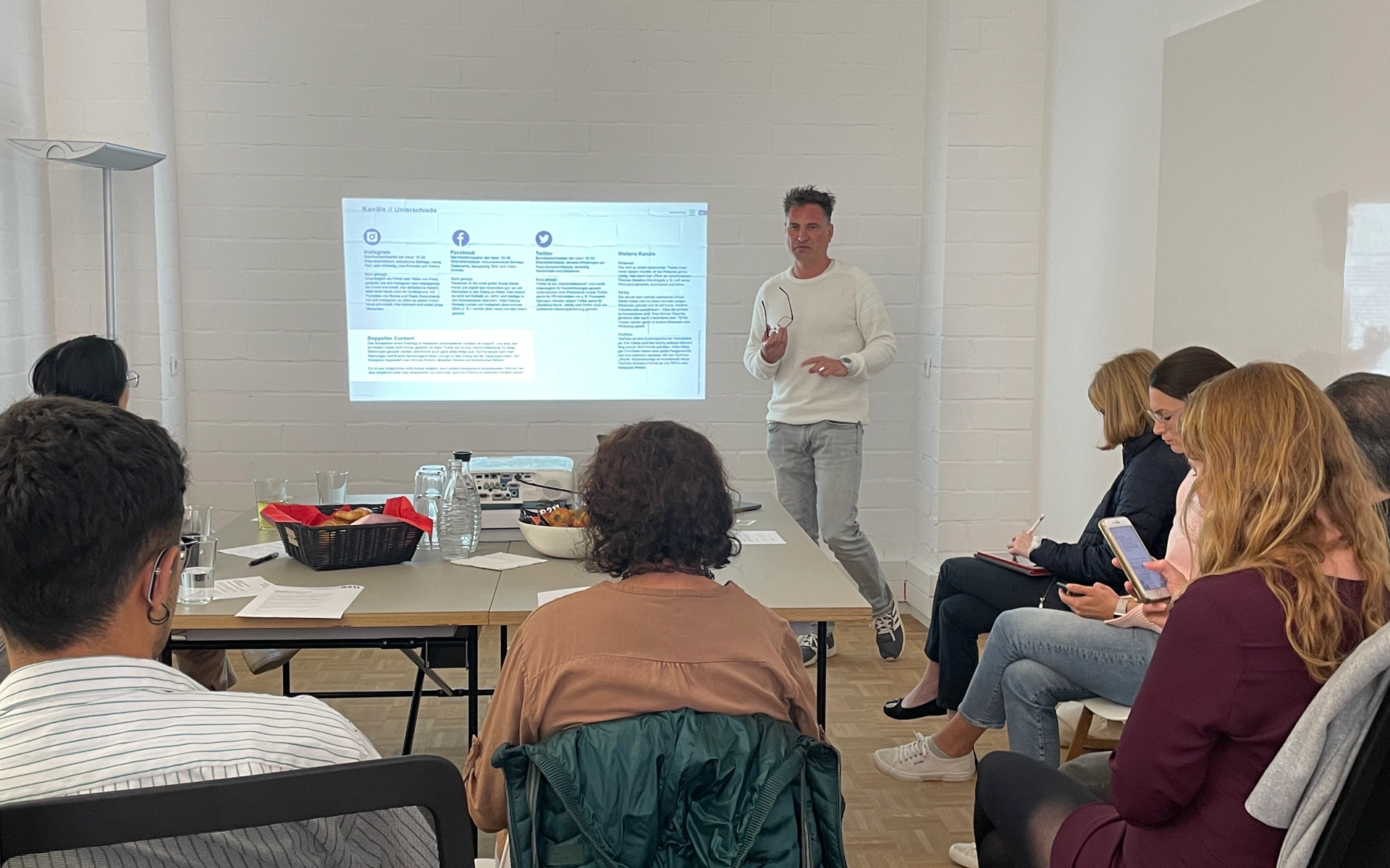 Aufnahme aus einem R211-Workshop zum Thema Marketing, B2B und Social Media: Eine Gruppe von Teilnehmenden folgt der Präsentation eines R211-Mitarbeitenden, der vor einem Screen Inhalte erläutert.