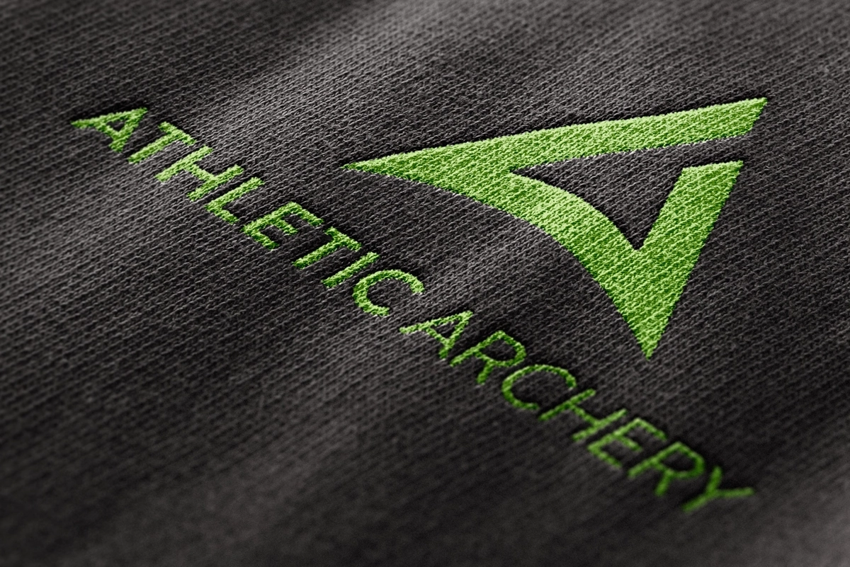 Aufnahme des Athletic Archery Logos als gestickte Version auf einem Shirt – als Beispiel für markengerechte Anwendung auf Textilien.