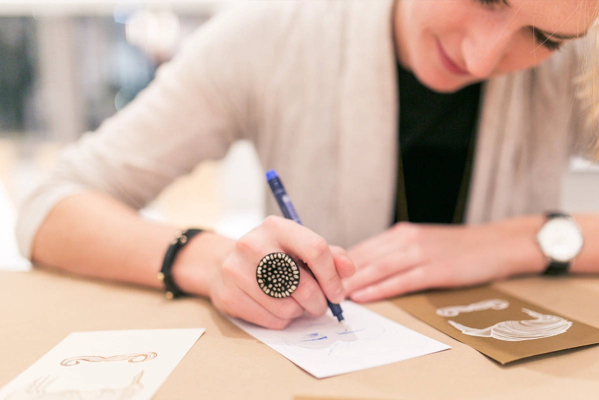 Nahaufnahme einer Eventbesucherin, die das präsentierte Papier testet und darauf schreibt. Aufnahme vom Paper Playground Event von Freytag & Petersen, visuell gestaltet von der R211-Agentur.