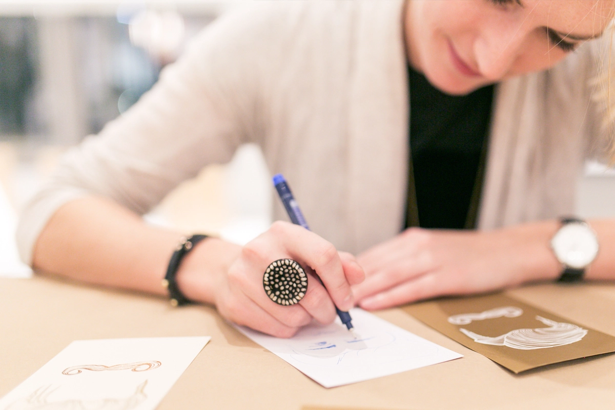 Nahaufnahme einer Eventbesucherin, die das präsentierte Papier testet und darauf schreibt. Aufnahme vom Paper Playground Event von Freytag & Petersen, visuell gestaltet von der R211-Agentur.