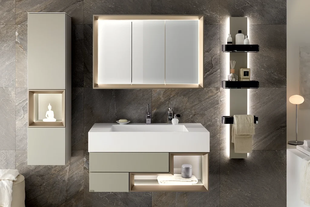 Modernes hülsta-Badezimmer mit beleuchtetem Spiegelschrank, Waschtisch und stilvollen Stauraumelementen vor Natursteinfliesen in warmen Tönen